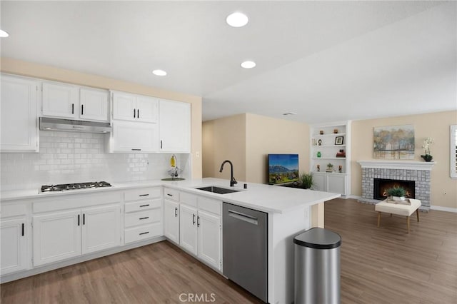 kitchen with a peninsula, gas stovetop, a sink, under cabinet range hood, and stainless steel dishwasher