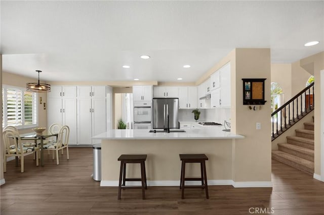 kitchen with a sink, dark wood-style floors, freestanding refrigerator, a peninsula, and white double oven