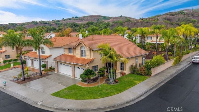 mediterranean / spanish house featuring stucco siding, driveway, a front lawn, a tile roof, and a mountain view