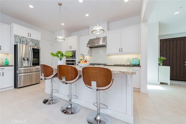 kitchen featuring under cabinet range hood, white cabinetry, stainless steel appliances, and a kitchen breakfast bar