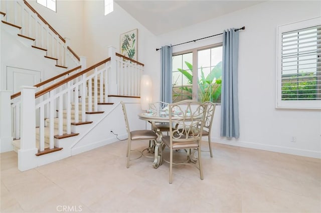 dining space featuring baseboards, a towering ceiling, and stairs