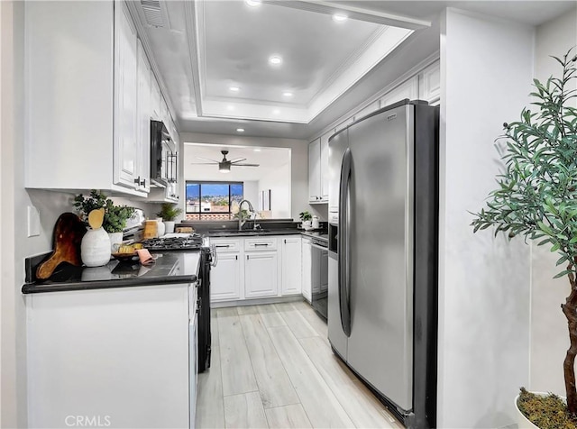 kitchen featuring a sink, dark countertops, white cabinetry, appliances with stainless steel finishes, and a raised ceiling