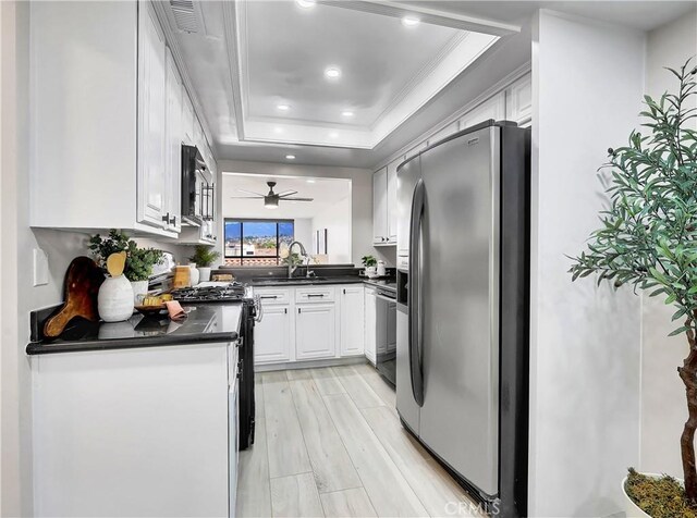 kitchen with dark countertops, recessed lighting, white cabinetry, a tray ceiling, and stainless steel appliances
