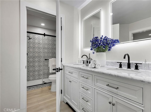 bathroom with a sink, toilet, double vanity, and a tile shower