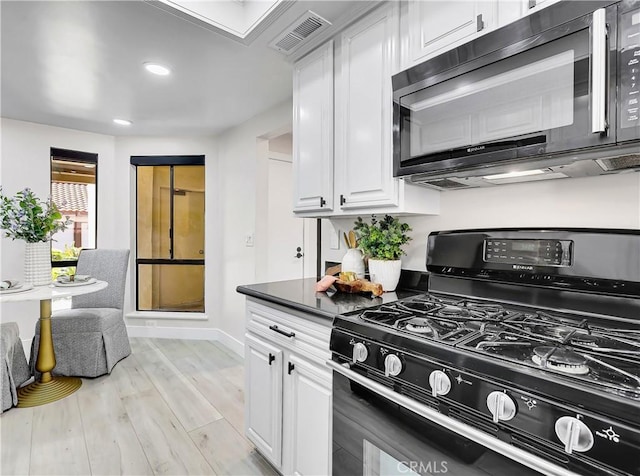 kitchen featuring baseboards, visible vents, light wood finished floors, black appliances, and white cabinets