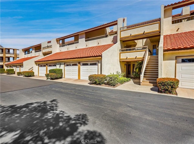 view of property with a tiled roof, a garage, concrete driveway, stairs, and stucco siding