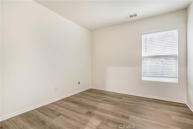 unfurnished room featuring wood finished floors, visible vents, and baseboards