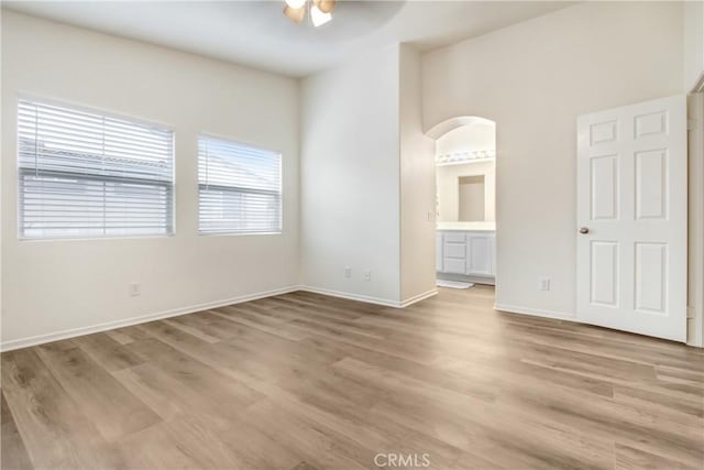 unfurnished bedroom featuring light wood-style floors, baseboards, ensuite bathroom, and arched walkways