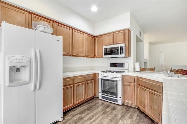 kitchen featuring tile counters, light wood-style flooring, a peninsula, white appliances, and a sink