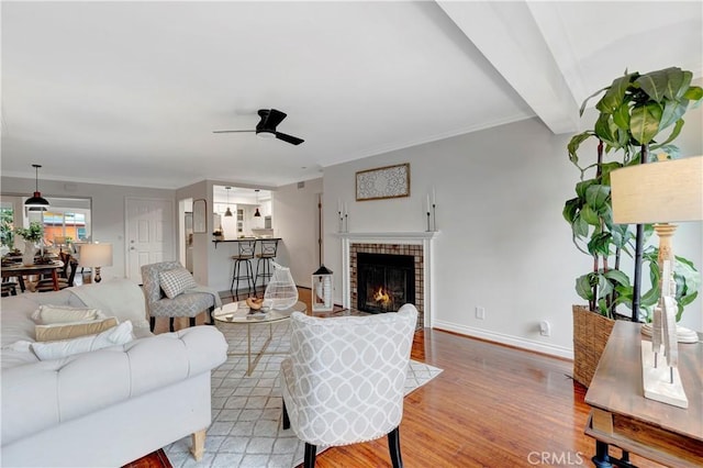 living area with wood finished floors, baseboards, a ceiling fan, beam ceiling, and a fireplace