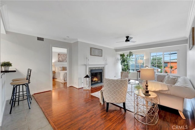 living area with visible vents, a fireplace, wood finished floors, and ornamental molding