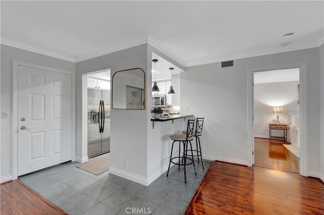 kitchen featuring visible vents, a breakfast bar area, ornamental molding, appliances with stainless steel finishes, and wood finished floors