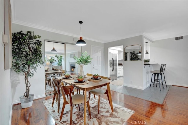 dining room featuring visible vents, a warm lit fireplace, crown molding, and light wood-style floors