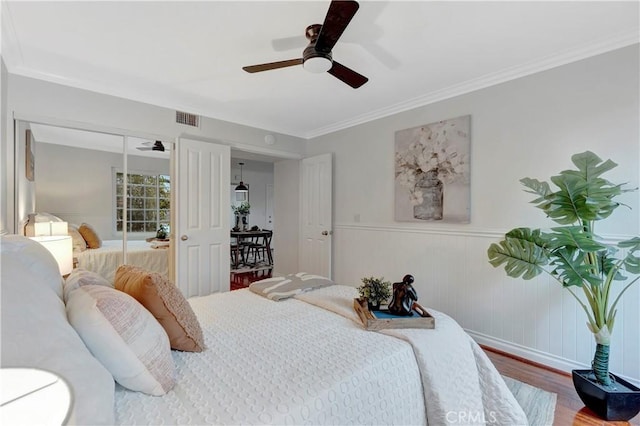 bedroom with visible vents, crown molding, ceiling fan, a wainscoted wall, and wood finished floors