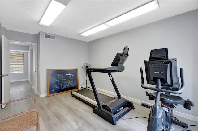 exercise area featuring light wood-type flooring, baseboards, visible vents, and a textured ceiling