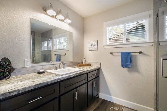 full bath with baseboards, wood finished floors, a stall shower, a textured wall, and vanity