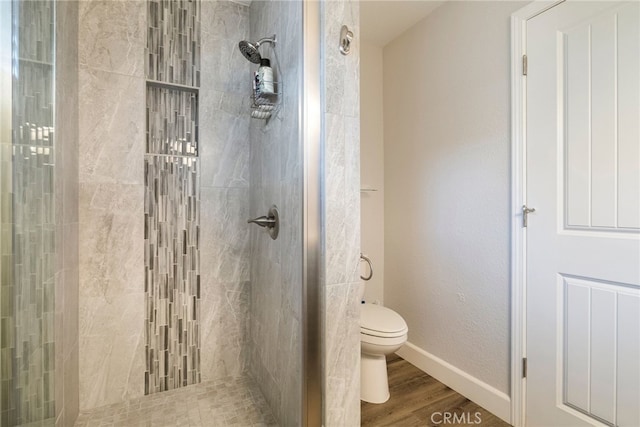 bathroom featuring baseboards, tiled shower, toilet, and wood finished floors