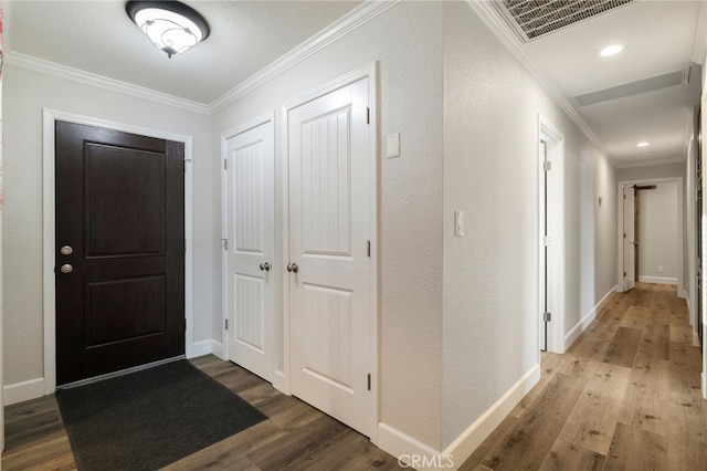 entryway featuring visible vents, crown molding, baseboards, wood finished floors, and a textured wall