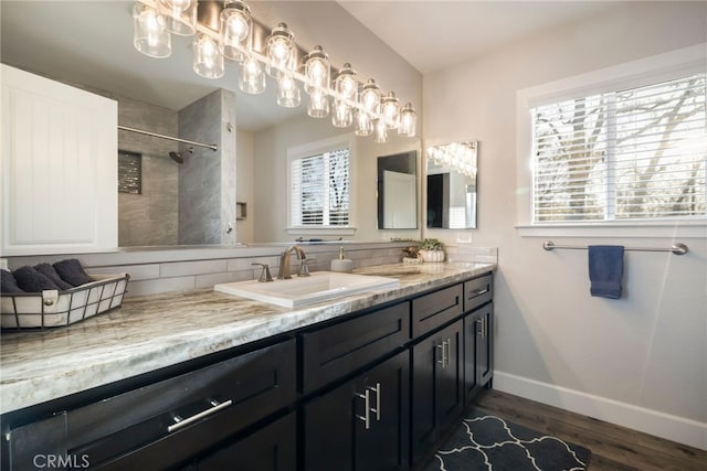 bathroom with baseboards, double vanity, tiled shower, wood finished floors, and a sink