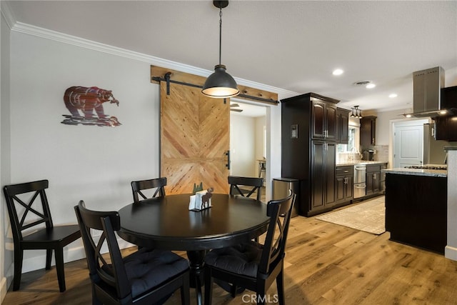 dining space featuring light wood finished floors, crown molding, baseboards, a barn door, and recessed lighting