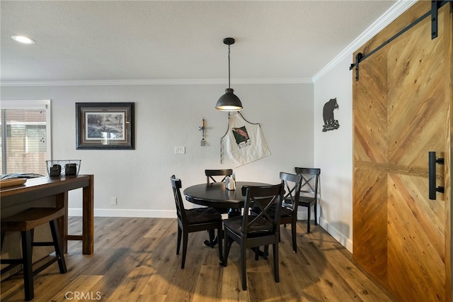 dining space featuring crown molding, baseboards, a barn door, wood finished floors, and a textured ceiling