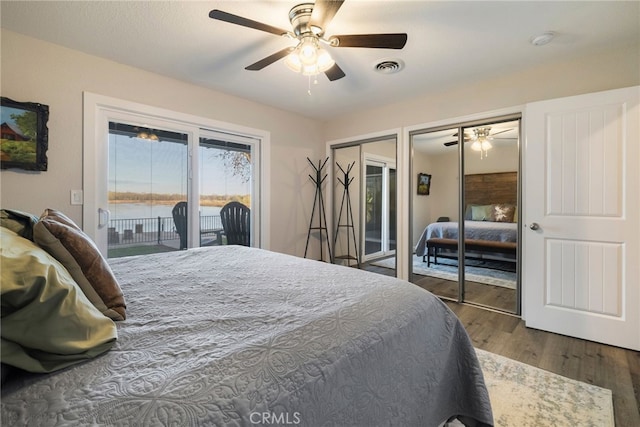 bedroom featuring access to exterior, visible vents, multiple closets, a water view, and wood finished floors