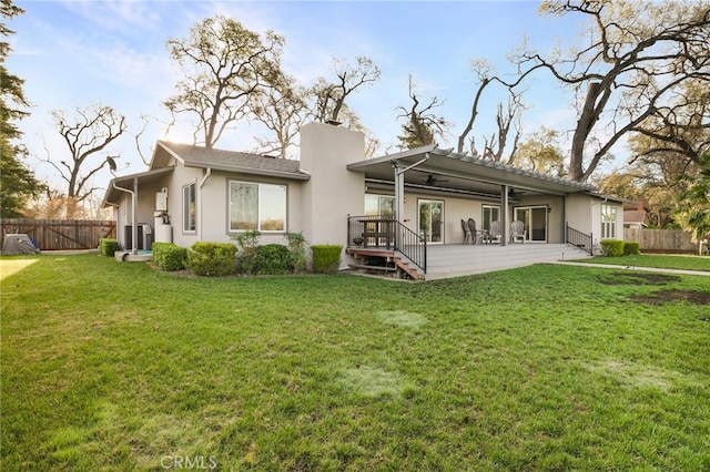 back of house featuring stucco siding, a lawn, a ceiling fan, fence, and a chimney