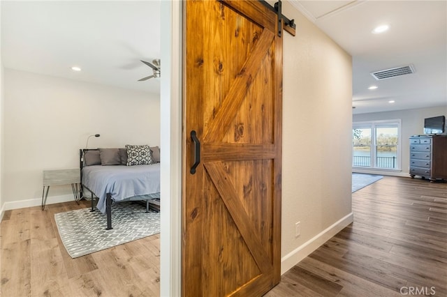 corridor featuring visible vents, baseboards, a barn door, and wood finished floors