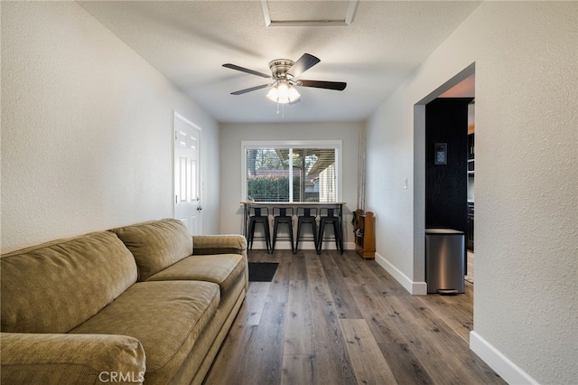 living area featuring baseboards, ceiling fan, hardwood / wood-style flooring, a textured ceiling, and a textured wall