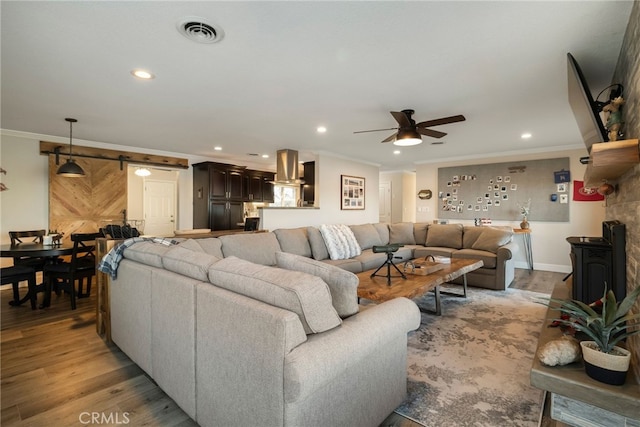 living area featuring visible vents, crown molding, a barn door, recessed lighting, and light wood-style flooring