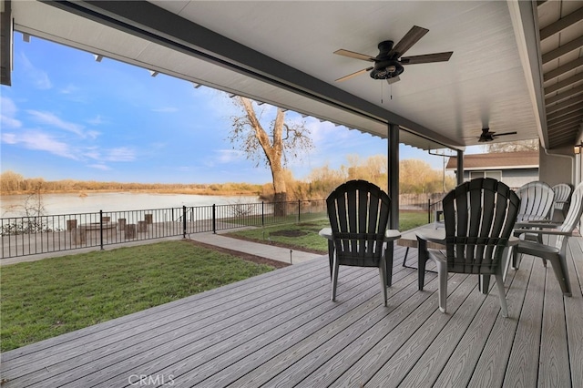 wooden terrace with a water view, a lawn, ceiling fan, and fence