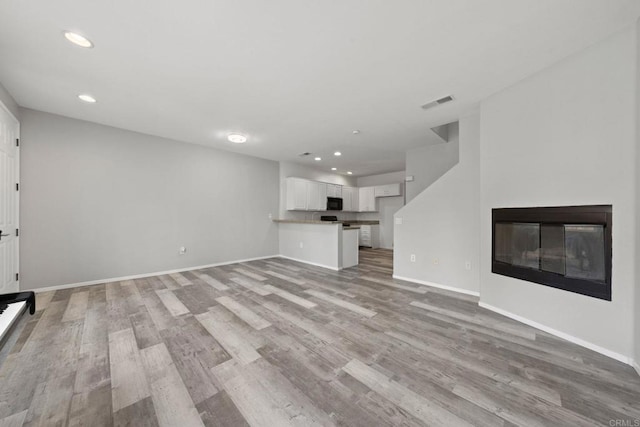 unfurnished living room featuring light wood finished floors, visible vents, baseboards, recessed lighting, and a glass covered fireplace