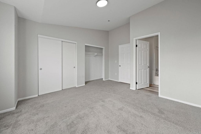 unfurnished bedroom with lofted ceiling, carpet, baseboards, and two closets