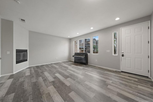 unfurnished living room with visible vents, wood finished floors, baseboards, and a glass covered fireplace