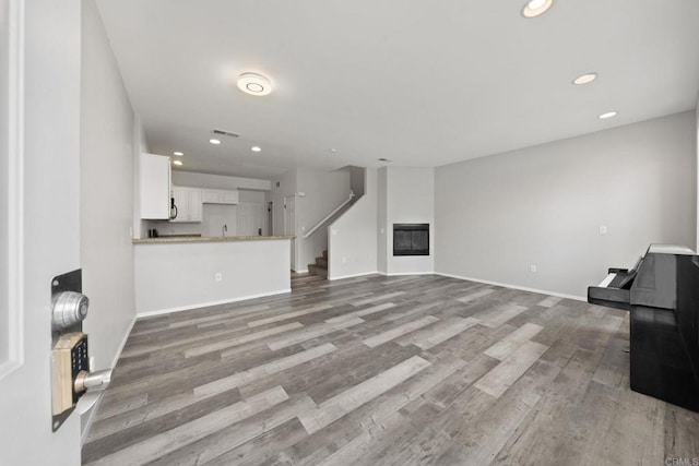 unfurnished living room with a glass covered fireplace, recessed lighting, baseboards, and wood finished floors