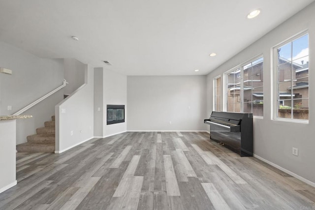 unfurnished living room with baseboards, stairs, recessed lighting, wood finished floors, and a glass covered fireplace