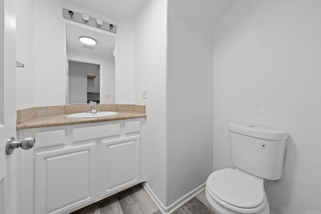 half bathroom with vanity, wood finished floors, visible vents, baseboards, and toilet