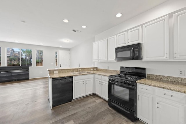 kitchen featuring visible vents, black appliances, a peninsula, white cabinetry, and a sink