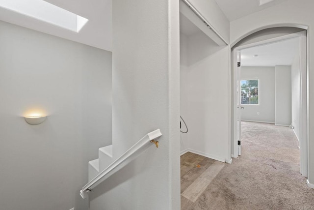 hall featuring an upstairs landing, a skylight, baseboards, and carpet floors