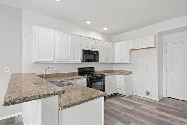 kitchen with light wood-type flooring, black appliances, a sink, a peninsula, and white cabinets