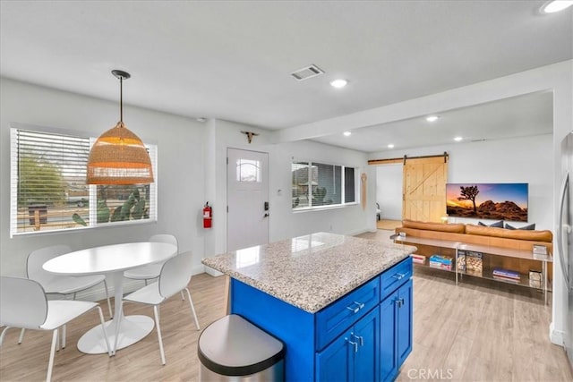 kitchen with visible vents, blue cabinetry, a kitchen island, a barn door, and light wood-style floors