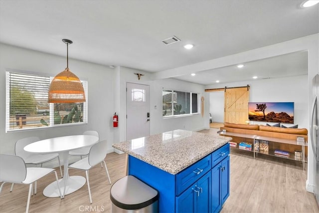 6566 El Rey Ave Unit 29, Palms, CA 92277 - kitchen with visible vents, a barn door, light wood finished floors, blue cabinetry, and a kitchen island