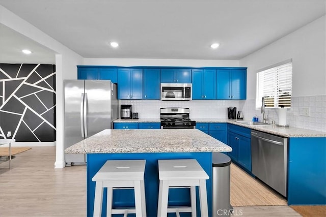 kitchen with a kitchen island, blue cabinetry, a sink, appliances with stainless steel finishes, and light wood-type flooring