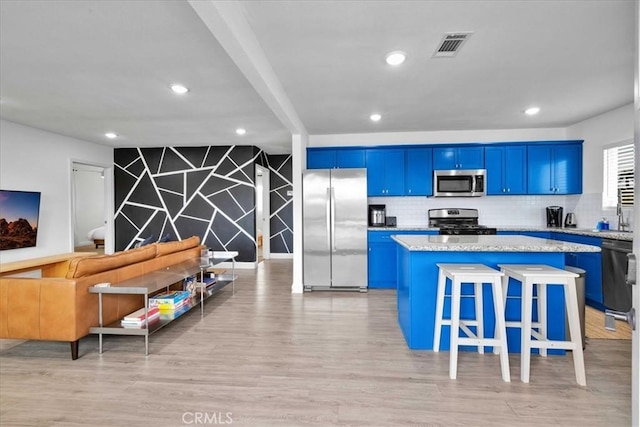 kitchen with blue cabinetry, a center island, an accent wall, light wood-style flooring, and stainless steel appliances