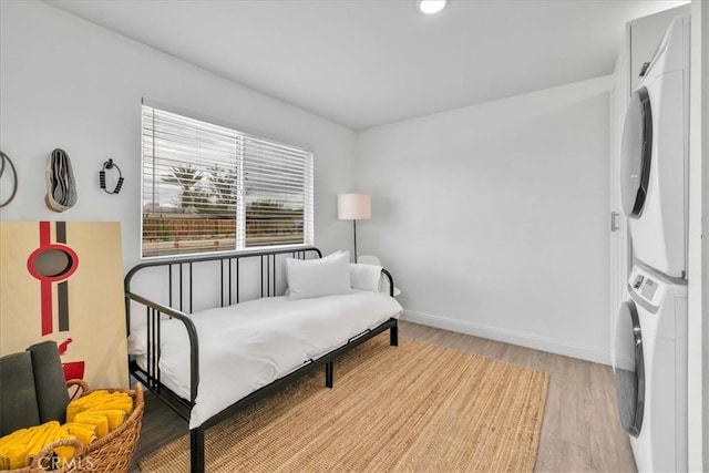 sitting room with light wood-style flooring, baseboards, and stacked washing maching and dryer