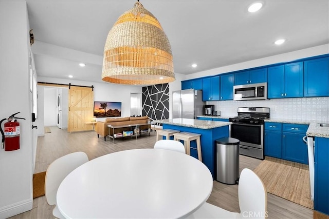 kitchen with tasteful backsplash, blue cabinetry, open floor plan, a barn door, and appliances with stainless steel finishes