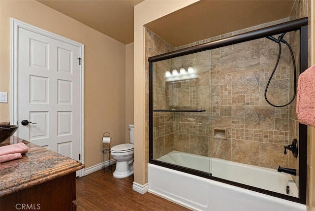 full bathroom featuring vanity, wood finished floors, baseboards, bath / shower combo with glass door, and toilet