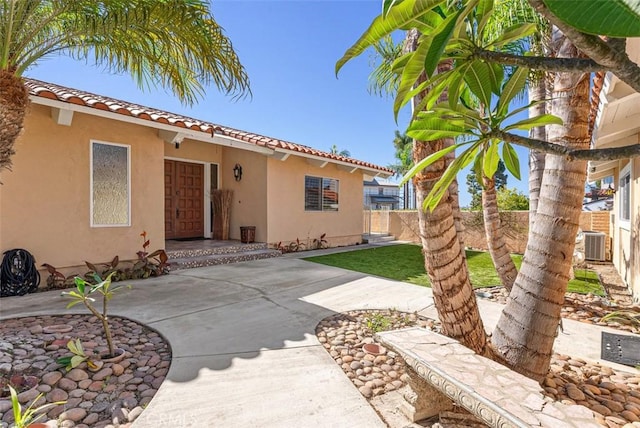 rear view of house with a tile roof, central air condition unit, fence, and stucco siding