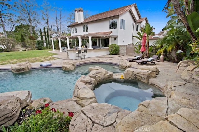 view of swimming pool featuring outdoor dry bar, a pool with connected hot tub, a pergola, a patio, and fence