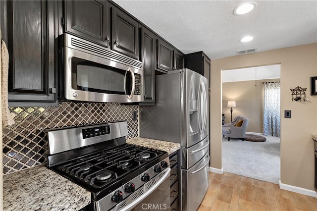 kitchen with visible vents, tasteful backsplash, dark cabinetry, appliances with stainless steel finishes, and baseboards